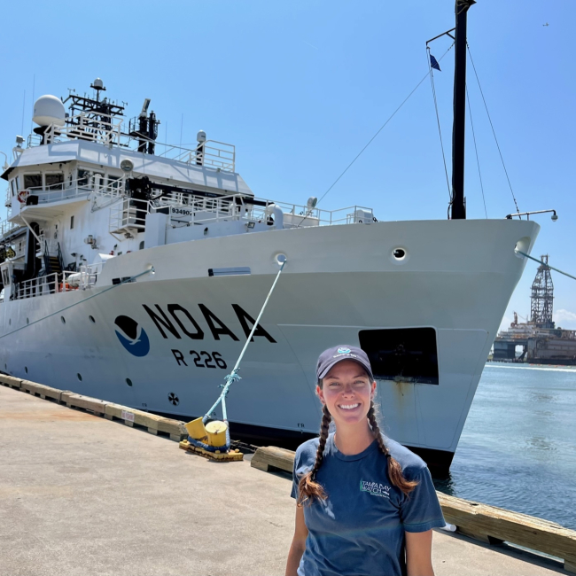 Jordan Findley poses in front of NOAA Ship Pisces at port. 