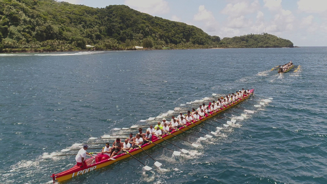 Traditional fautasi race on the ocean near land in American Samoa. Each boat has about 40 paddlers.